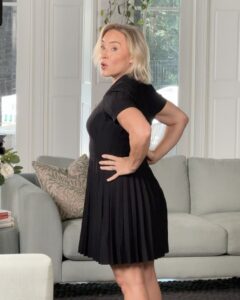 Kate at home in a black short-sleeved pleated dress rented through Rent the Runway.